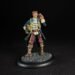 Miniature pirate captain in a blue coat with yellow trim, holding a telescope to his eye, standing on a textured circular base.