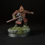 Miniature dwarf warrior in red armor wielding a double-headed axe on a rocky grassy base, black background.