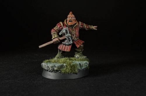 Miniature dwarf warrior in red armor wielding a double-headed axe on a rocky grassy base, black background.