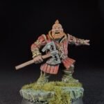Miniature dwarf warrior with orange beard in red armor, holding a double-headed axe, standing on a grassy base.
