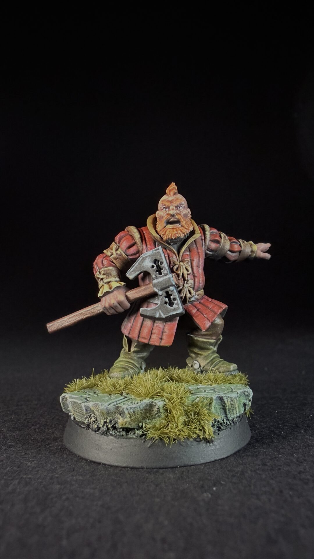 Miniature dwarf warrior with orange beard in red armor, holding a double-headed axe, standing on a grassy base.