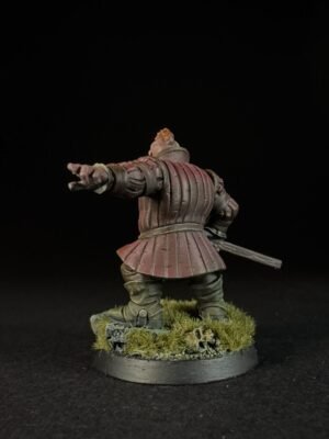 IMG_1496 Back view of a medieval knight miniature in red armor, with right arm extended as if pointing or gesturing, sword at the hip, standing on a grassy base.