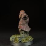 Painted miniature of a medieval knight in pink armor standing on a grassy base, facing forward with a pointed gesture.