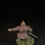 Rear view of a pink-armored medieval knight miniature, holding a sword, standing on a grassy base.