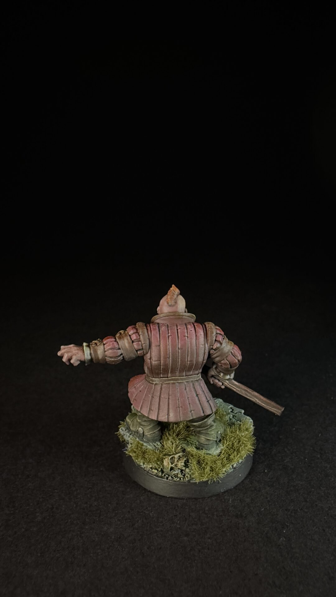 Rear view of a pink-armored medieval knight miniature, holding a sword, standing on a grassy base.