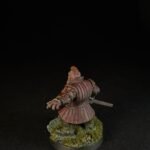 Back view of a medieval knight miniature in pinkish armor, with a sword at the side, standing on a grassy base.