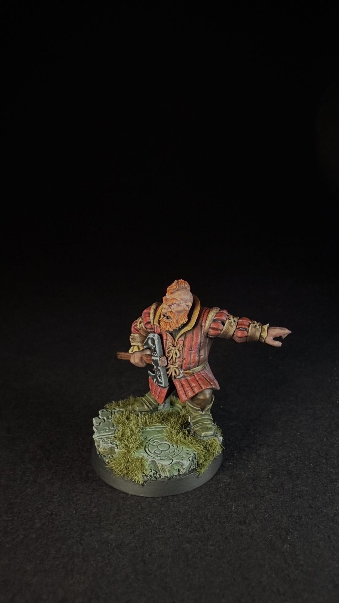 Fantasy dwarf miniature in red armor, wielding a war hammer with an outstretched left arm, standing on a grassy stone base.