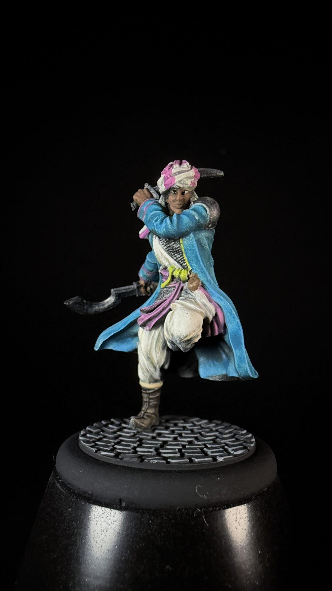 Colorful miniature pirate/warrior in blue coat and pink turban, wielding a curved sword on a textured base.