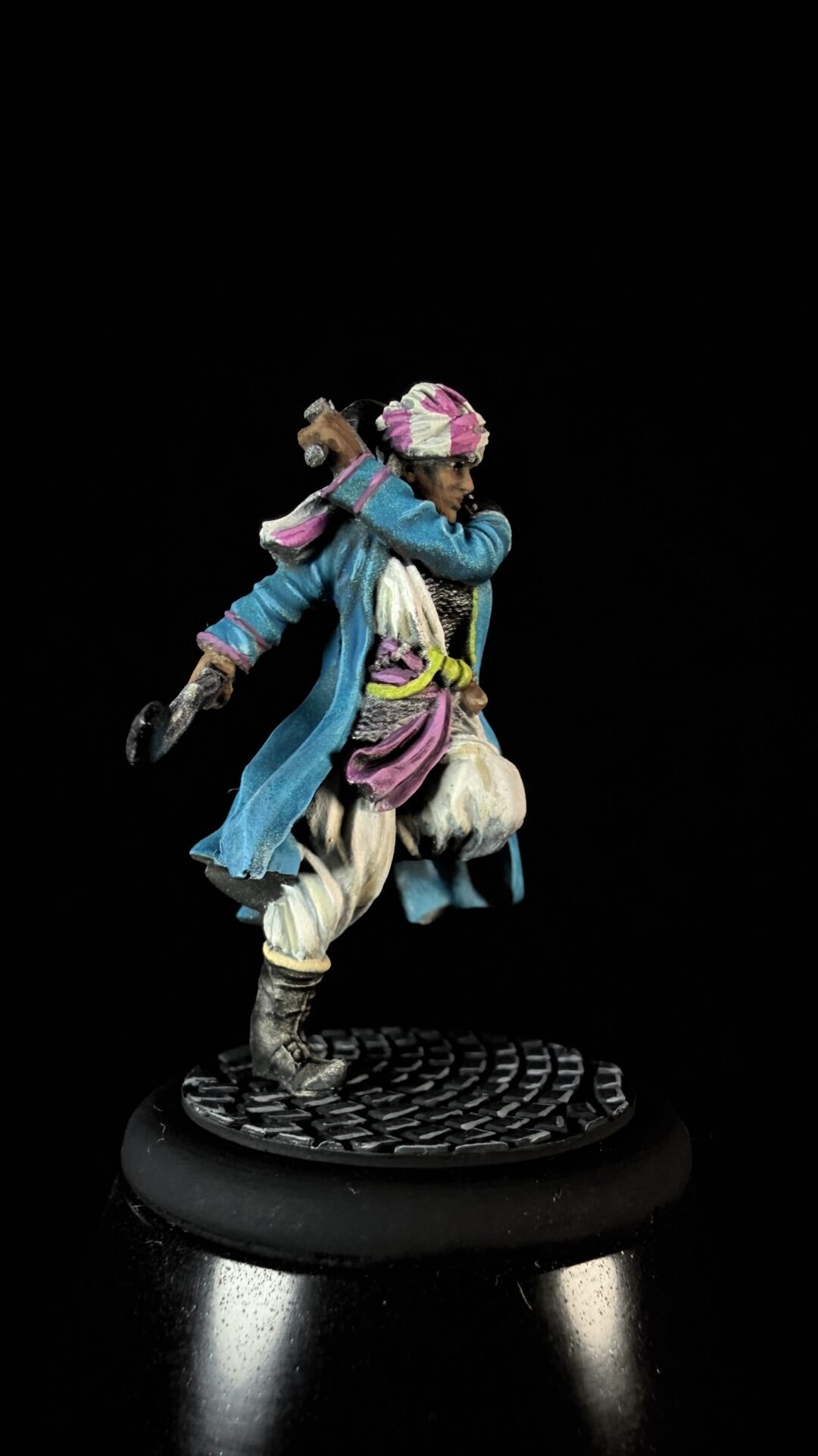 Detailed miniature of a sword-wielding pirate in a blue coat and pink turban, posed mid-stride on a textured base.