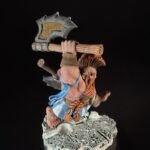 Fantasy miniature barbarian warrior swung over his head with a large double-headed axe, standing on a rocky base, wearing blue fabric and brown leather.