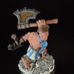Barbarian mini figure mid-stride, lifting a large ornate axe over his shoulder, wearing a blue-and-white striped kilt and brown accessories on a rocky base.