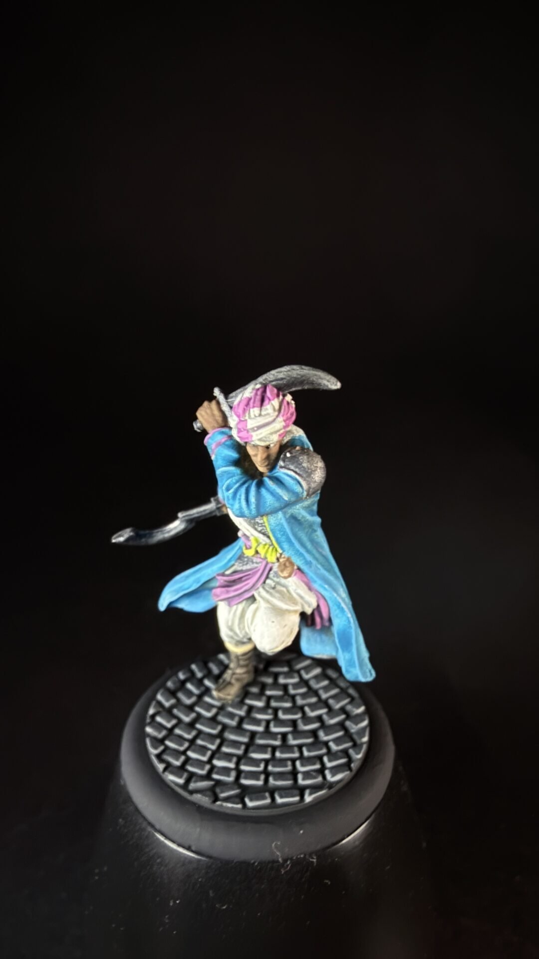Miniature pirate figure in a blue coat with a pink headscarf, wielding a curved saber on a textured round base