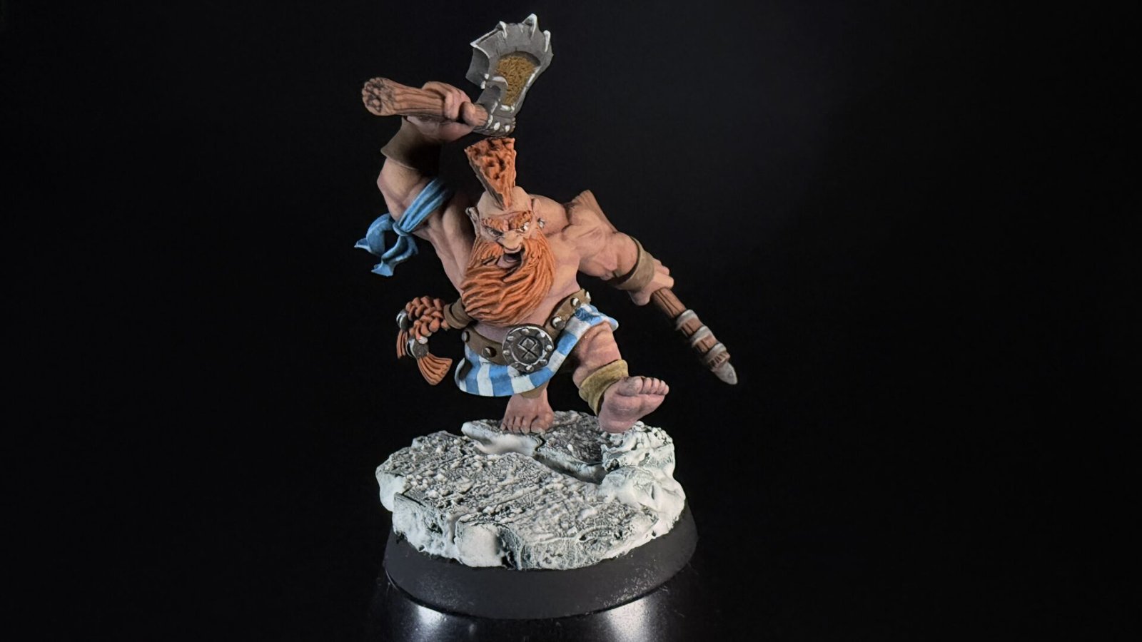 Painted dwarf barbarian miniature raising a battle-axe on a rocky base against a black background.