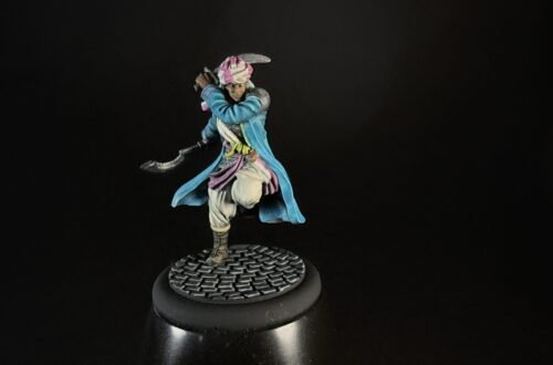 Tabletop miniature of a pirate-like fighter in a blue coat, pink scarf, and white pants, posed with a curved blade, standing on a cobblestone base against a dark background