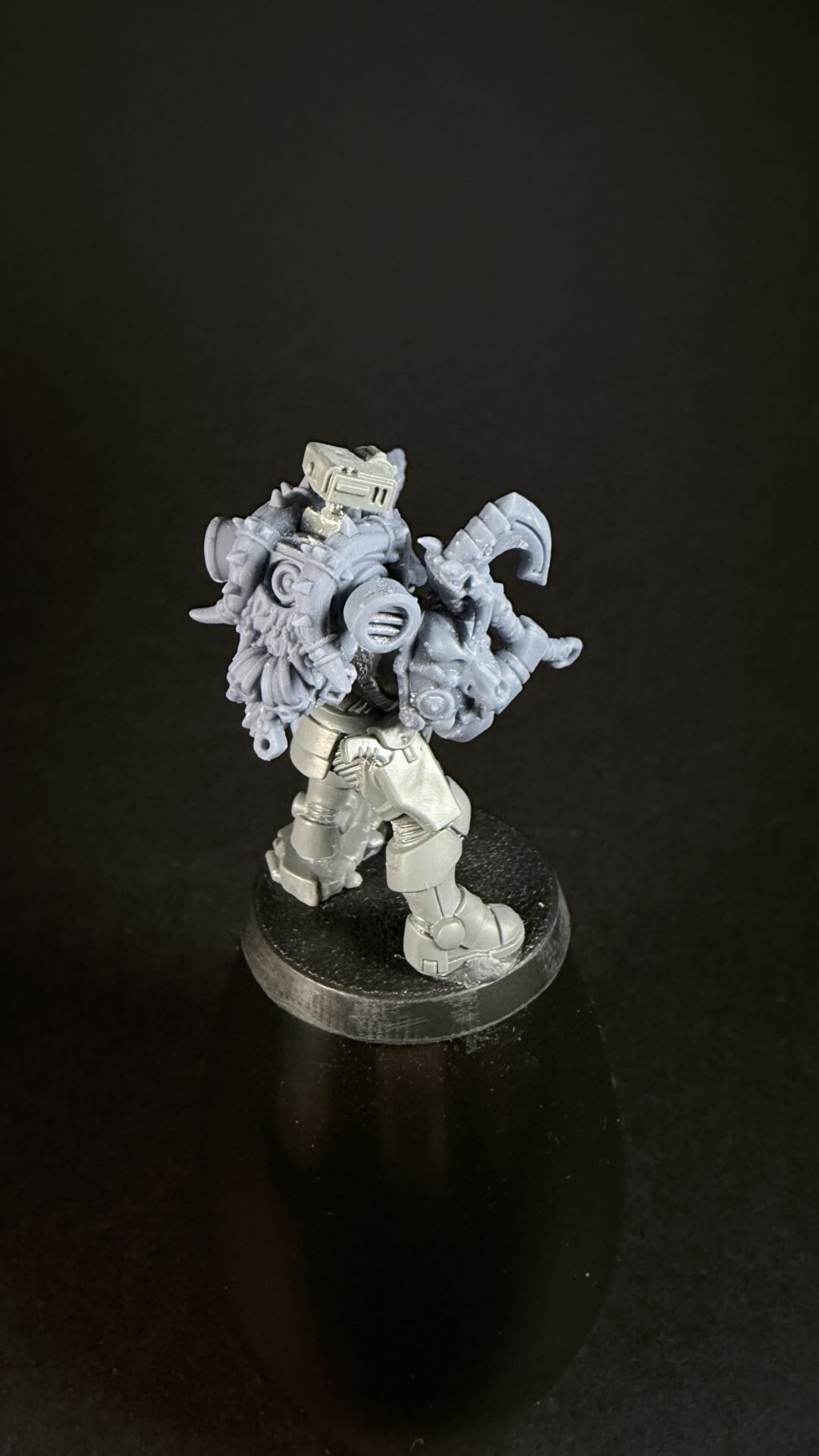 Grey sci-fi armored miniature with a large back-mounted gear unit, standing on a round base against a black background.