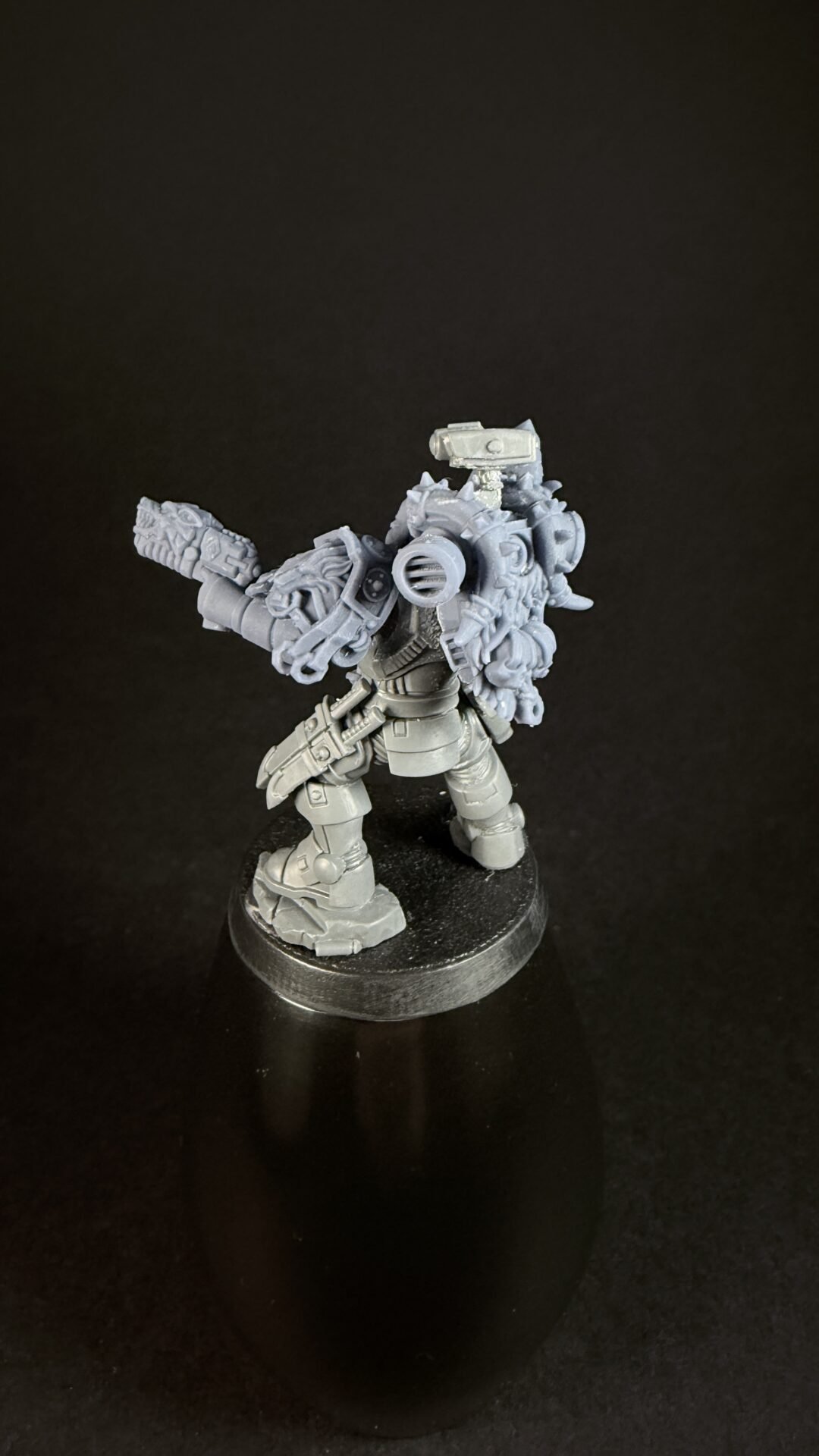 Unpainted gray miniature of a heavily armored sci‑fi soldier with a large backpack and gun, standing on a round base.