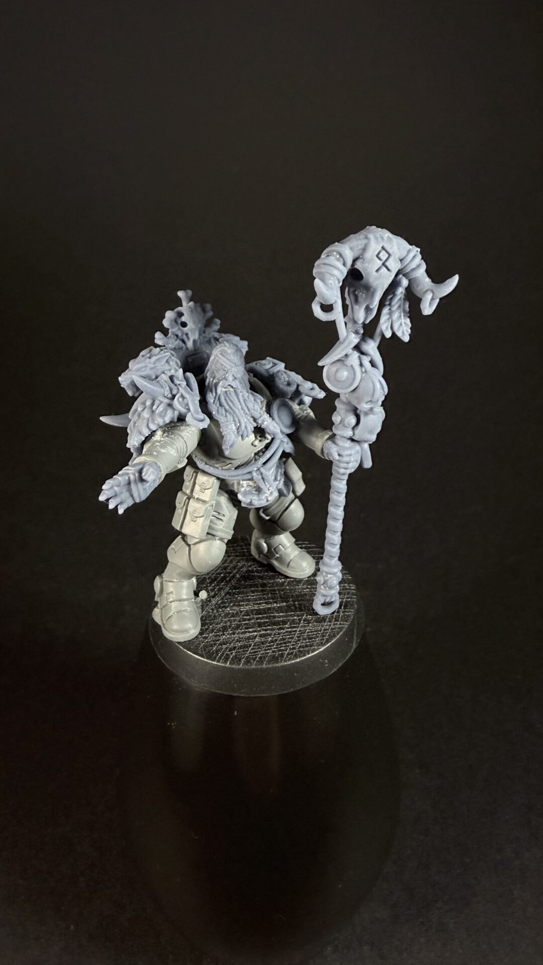 Unpainted fantasy miniature: a bulky armored warrior with horns, holding a tall carved staff, standing on a round textured base.