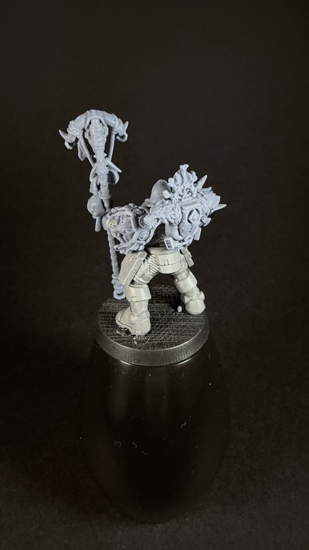 Tabletop miniature of a heavily armored orc-like figure holding a tall, spiked staff with skeletal shapes, standing on a round base.
