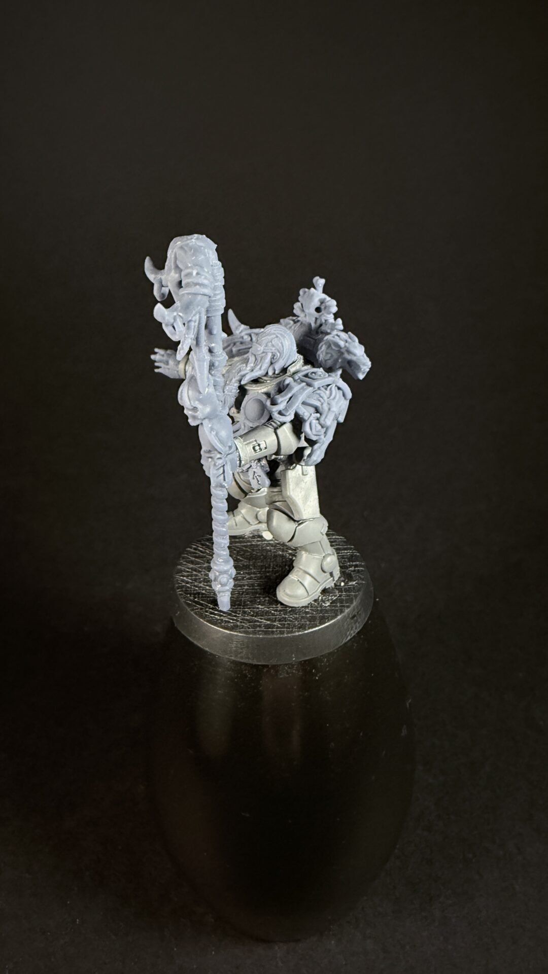 Grey plastic miniature of a heavily armored warrior gripping a tall, spiked staff, standing on a round textured base.