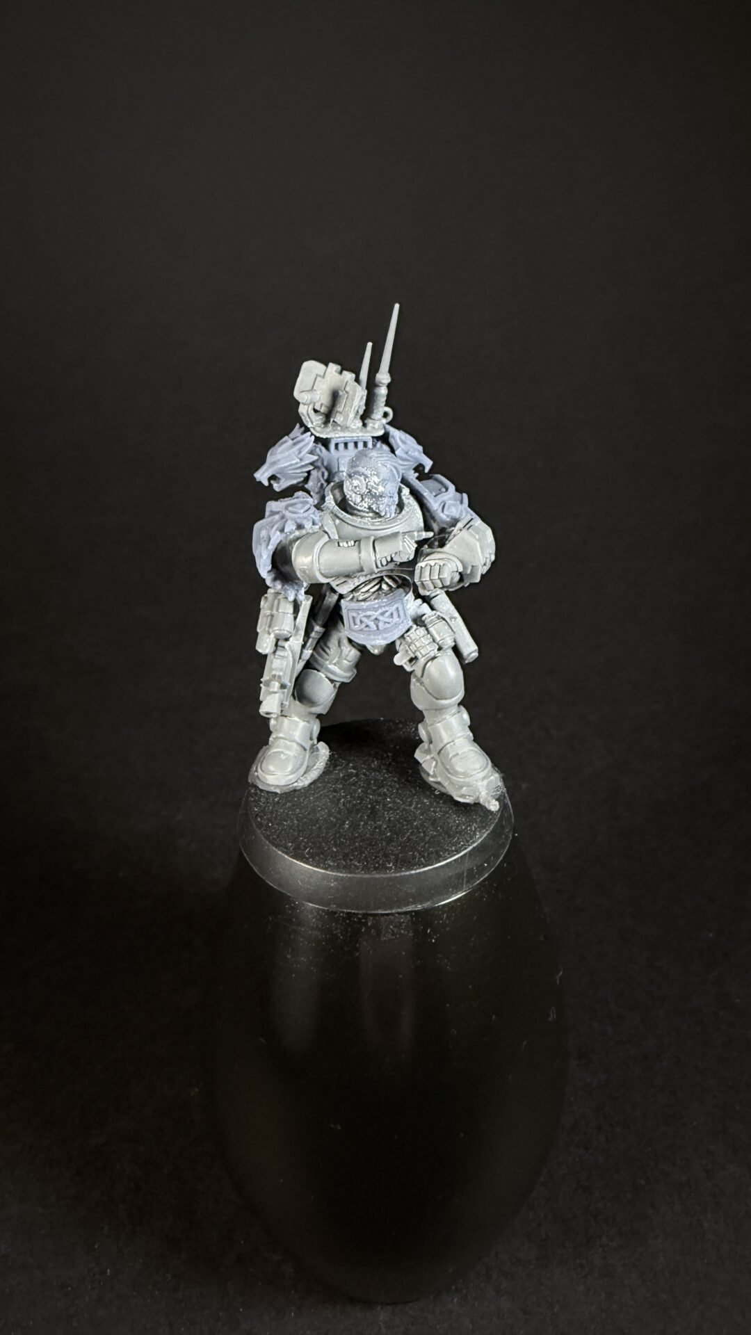 Gray sci‑fi armored warrior miniature standing on a black base, weapons mounted on back and clenched fists forward.