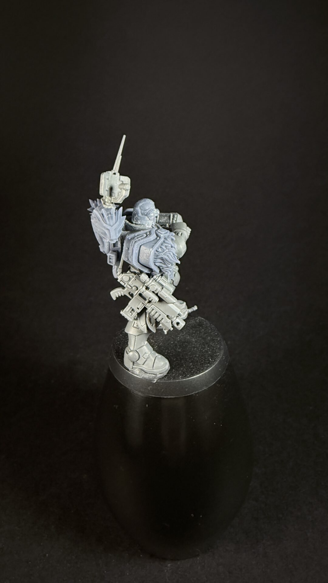 Grey sci-fi armored miniature posed with a raised melee weapon and large gun, on a round base.