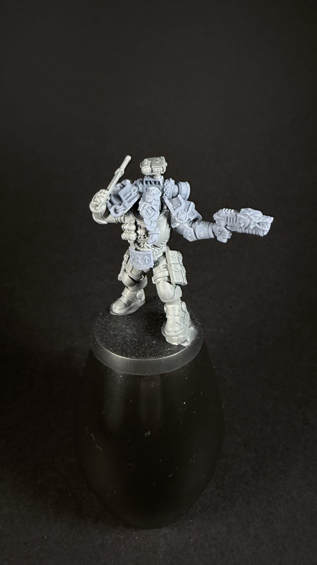 Unpainted gray sci‑fi armored miniature standing on a round base, holding a gun in the right hand and a melee weapon in the left.