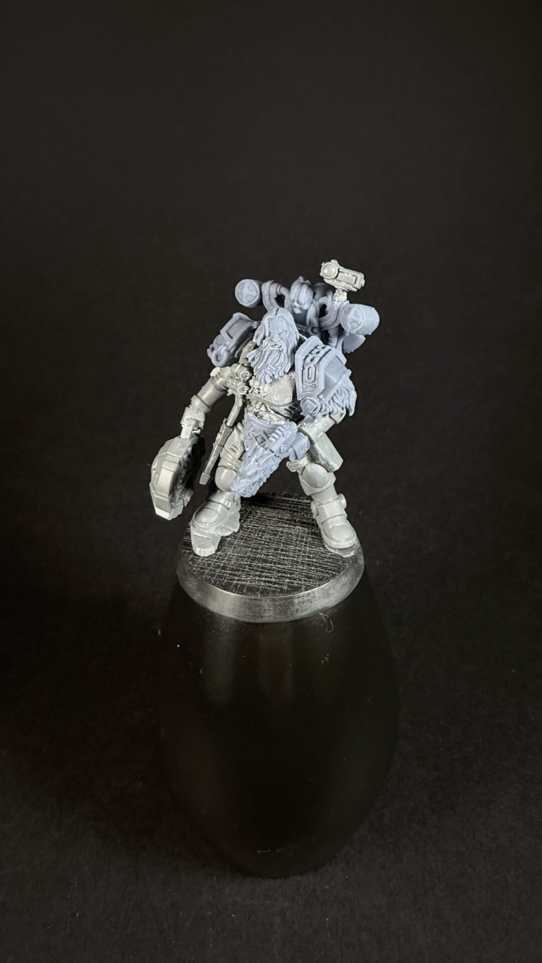 Unpainted grey plastic Warhammer 40k space marine miniature on a round textured base, armed with a bolt weapon and shoulder armor plates with a back-mounted pack.