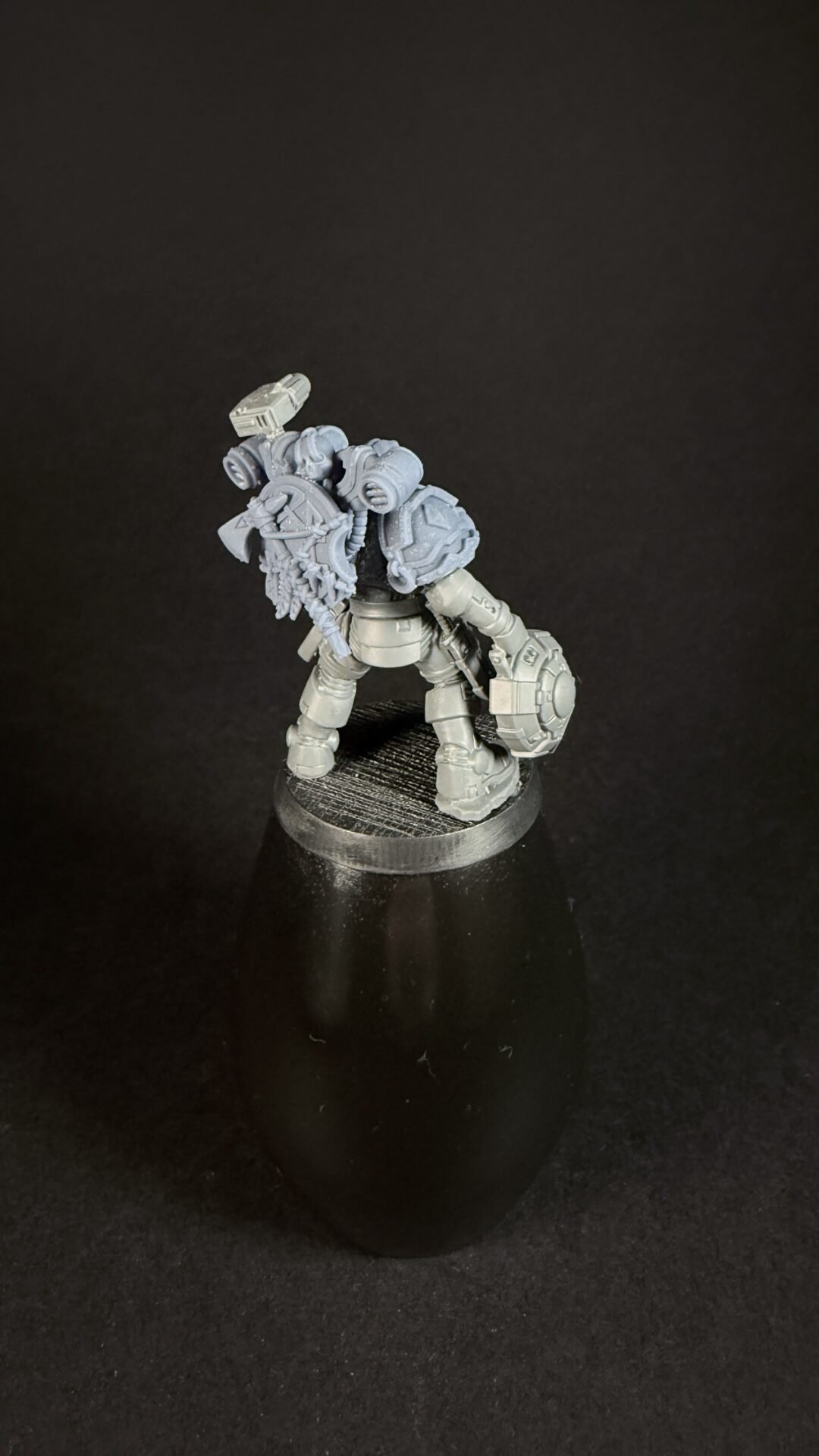 Unpainted gray plastic tabletop miniature of a armored warrior with a round shield and a spiked melee weapon, standing on a black display base.