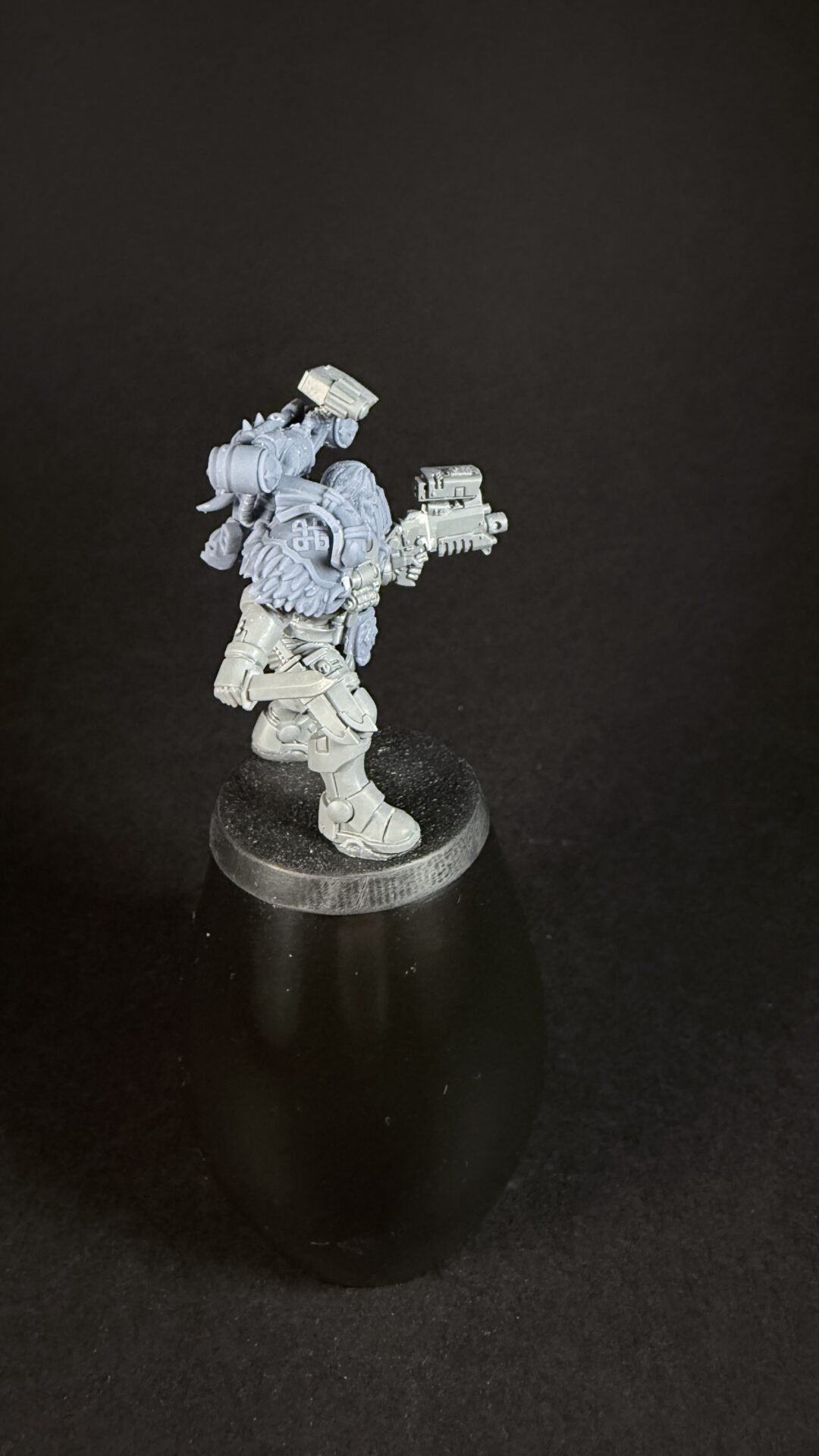 Unpainted gray sci-fi miniature figure in armor holding a blaster, standing on a round base against a black background.