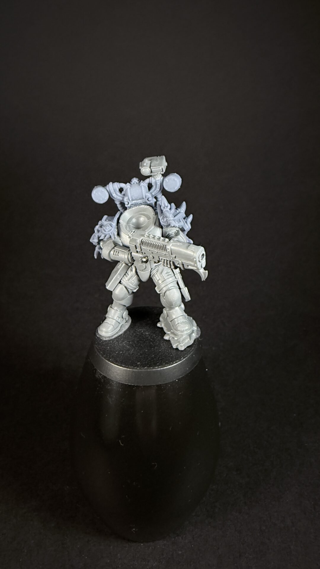 Unpainted sci-fi miniature in bulky armor, holding a large futuristic rifle, standing on a black display base