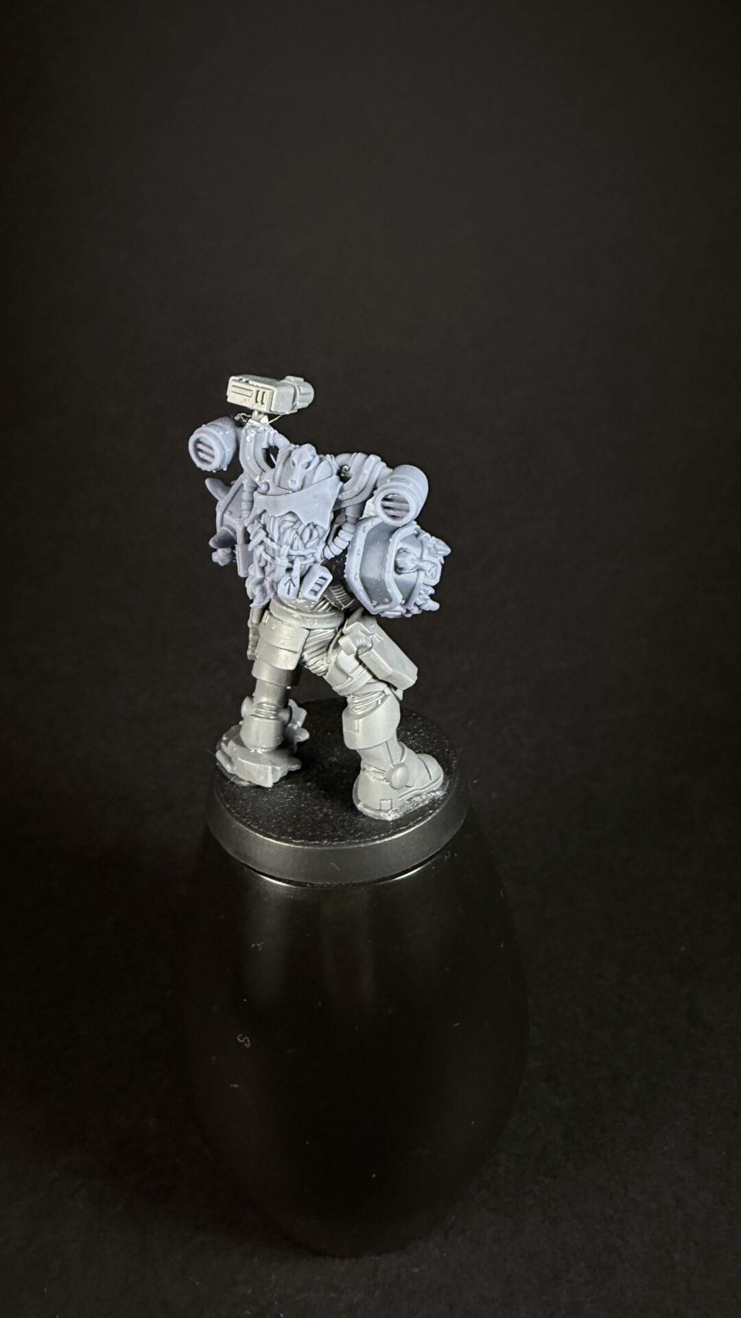 Unpainted gray plastic science-fiction armored miniature on a round base, with a bulky backpack and weapon.