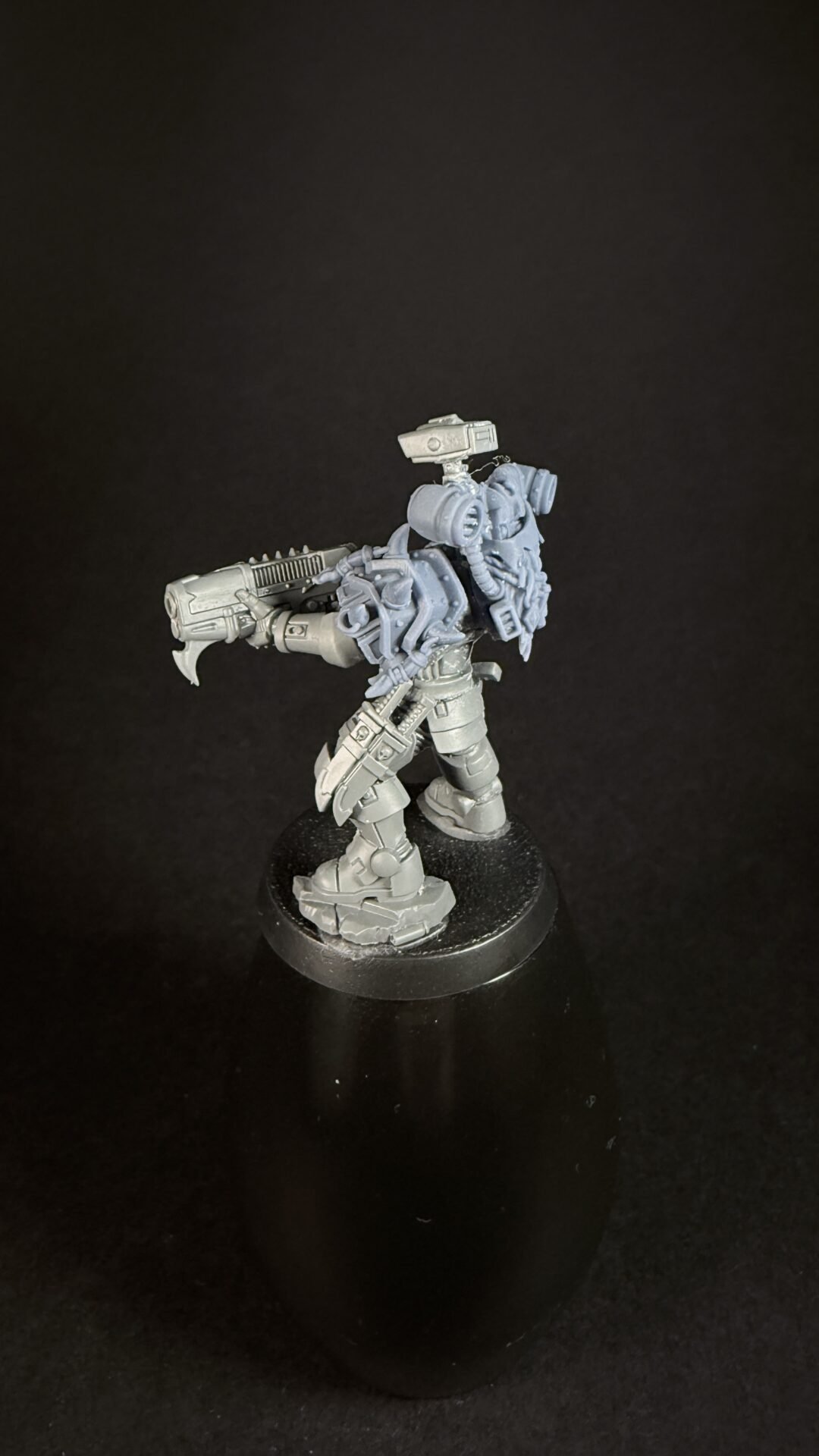 Gray sci-fi mech miniature in a dynamic firing pose with a large gun, mounted on a circular black base.