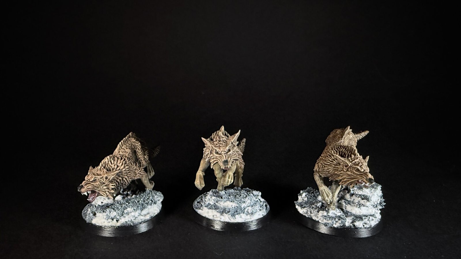 Three dragon miniatures on snowy bases arranged in a row against a black background, ready for tabletop gaming.