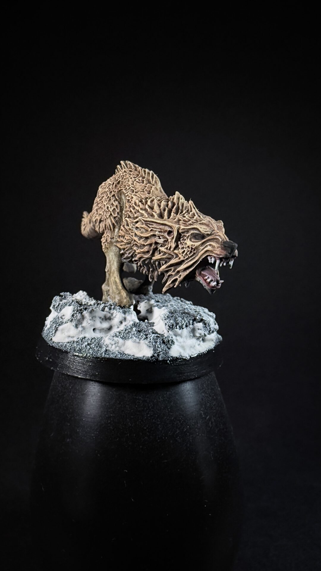 Miniature dragon head sculpture with intricate bone-like scales on a snowy rocky base, mouth open in a roar.