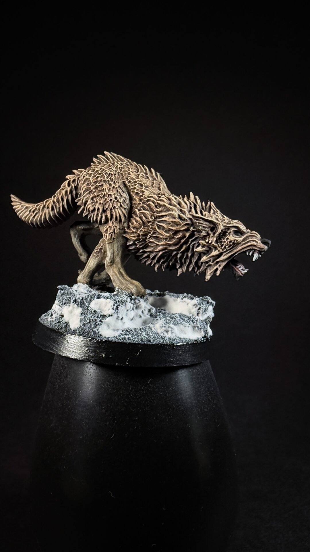 Detailed sculpture of a snarling wolf with jagged fur texture, standing on a snowy rocky base on a black background.
