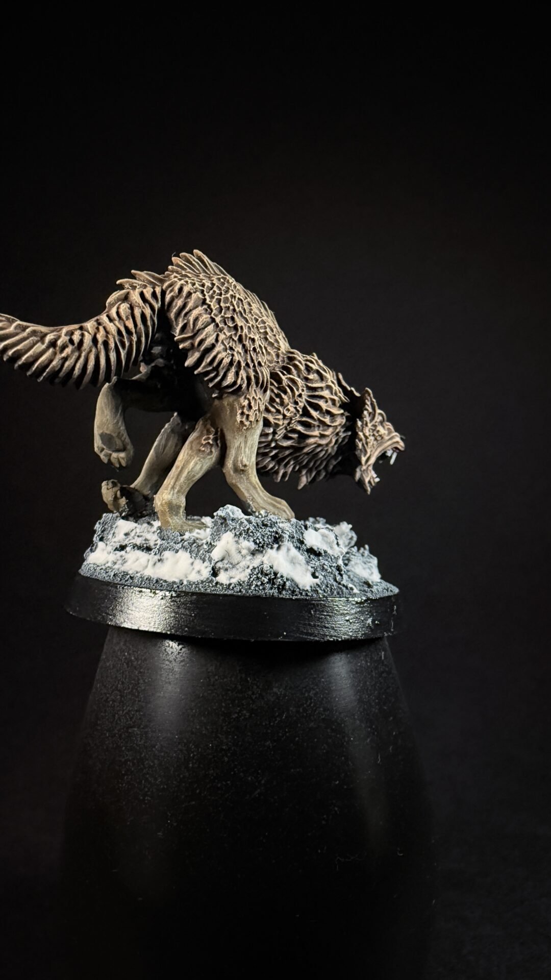 Intricately carved wolf sculpture with spiky fur on a snow-covered base against a black background.