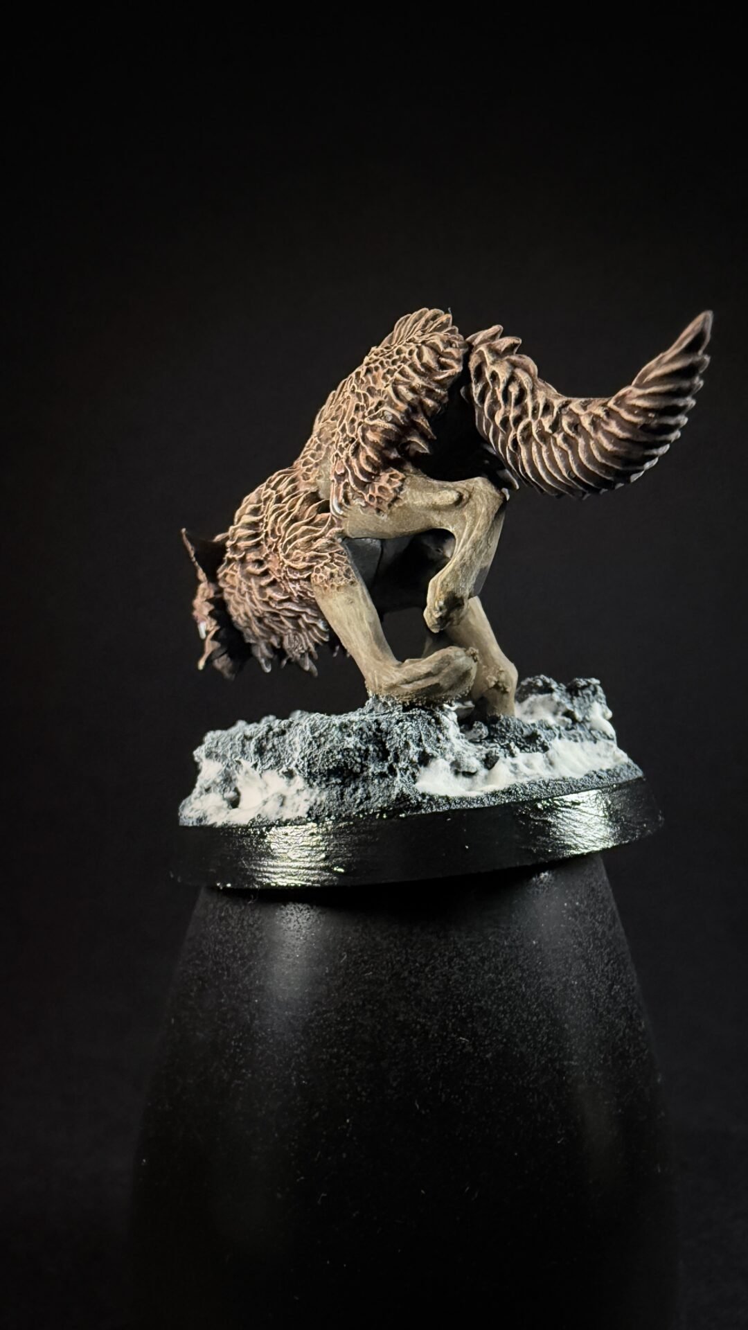 Fantasy griffin-like creature with large feathered wings crouching on a snow-dusted rocky base.
