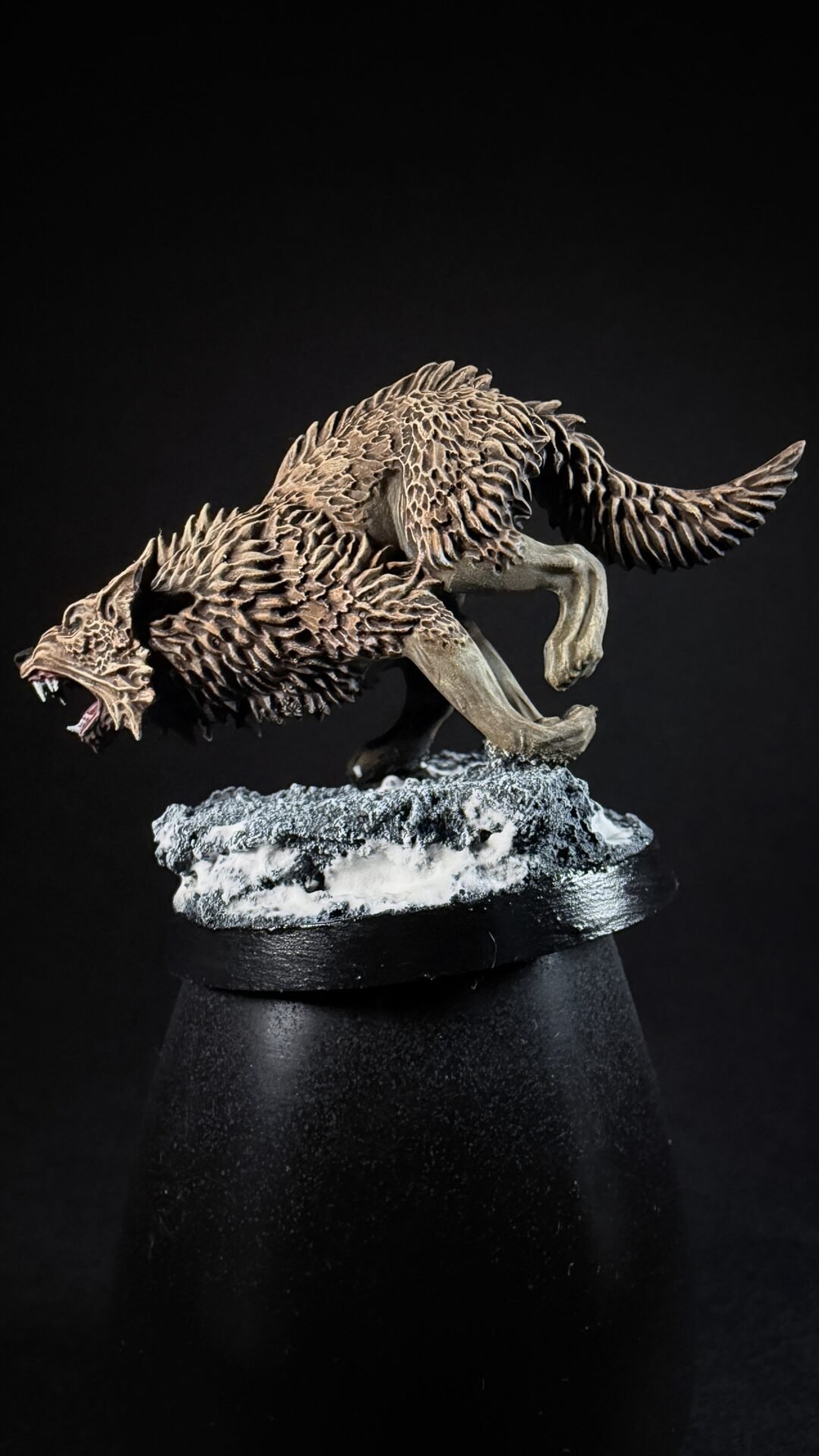 Detailed sculpture of a snarling wolf with jagged fur, posed as if leaping, on a frosted rocky base against a black background.