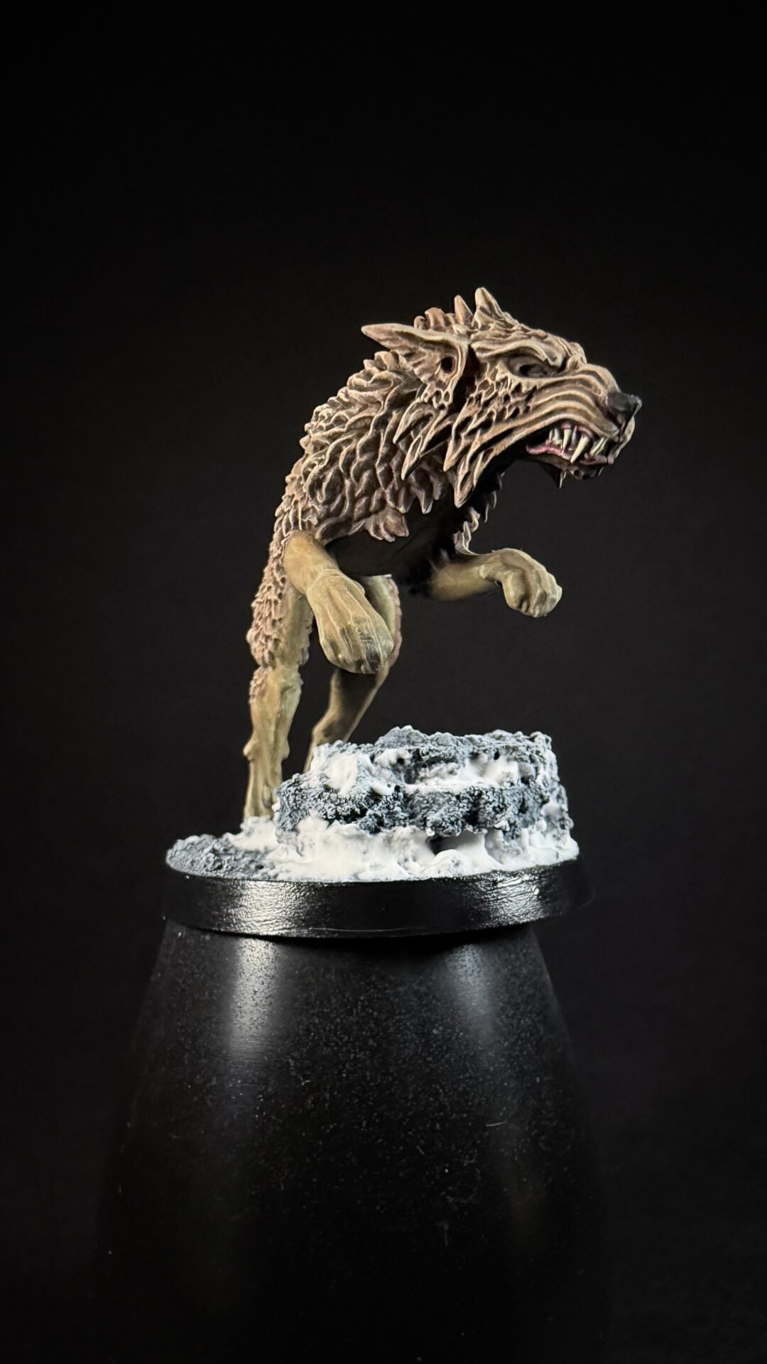 Miniature werewolf figure on a snowy rocky base, posed as if prowling forward, against a dark background.