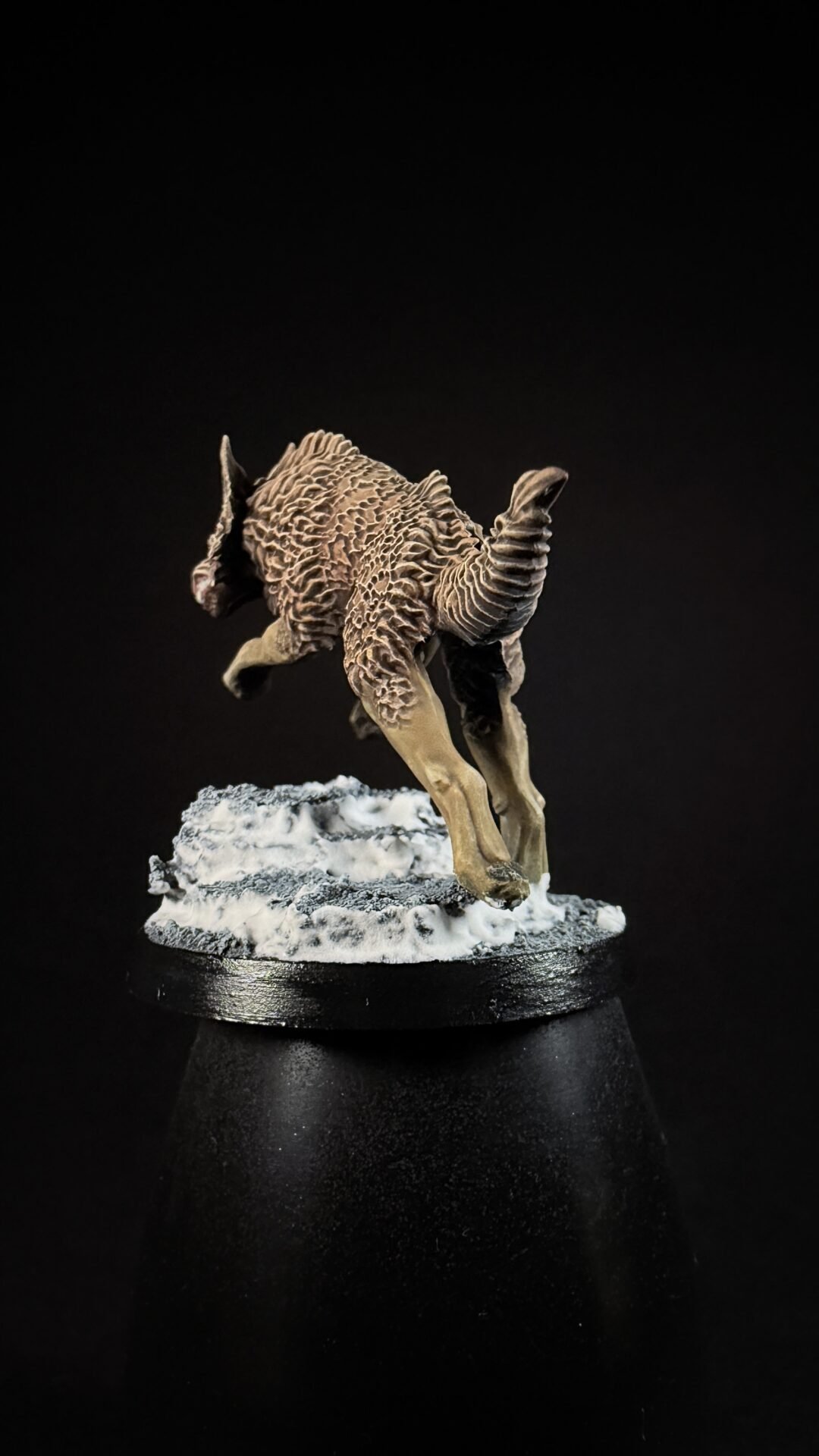 Miniature sculpted creature with shaggy ridged fur and curled horns, standing on a snow-covered base against a black background.