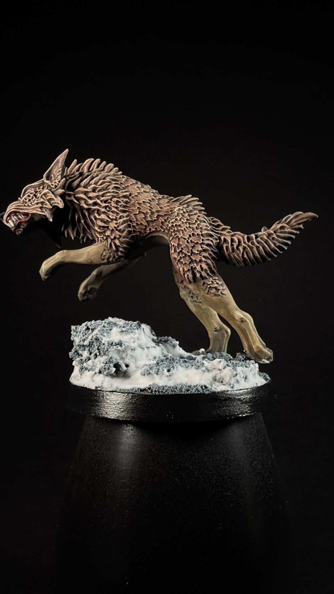 Brown, spiky-furred dragon-wolf sculpture mid-leap over a snowy rocky base on a black background, displayed on a stand.