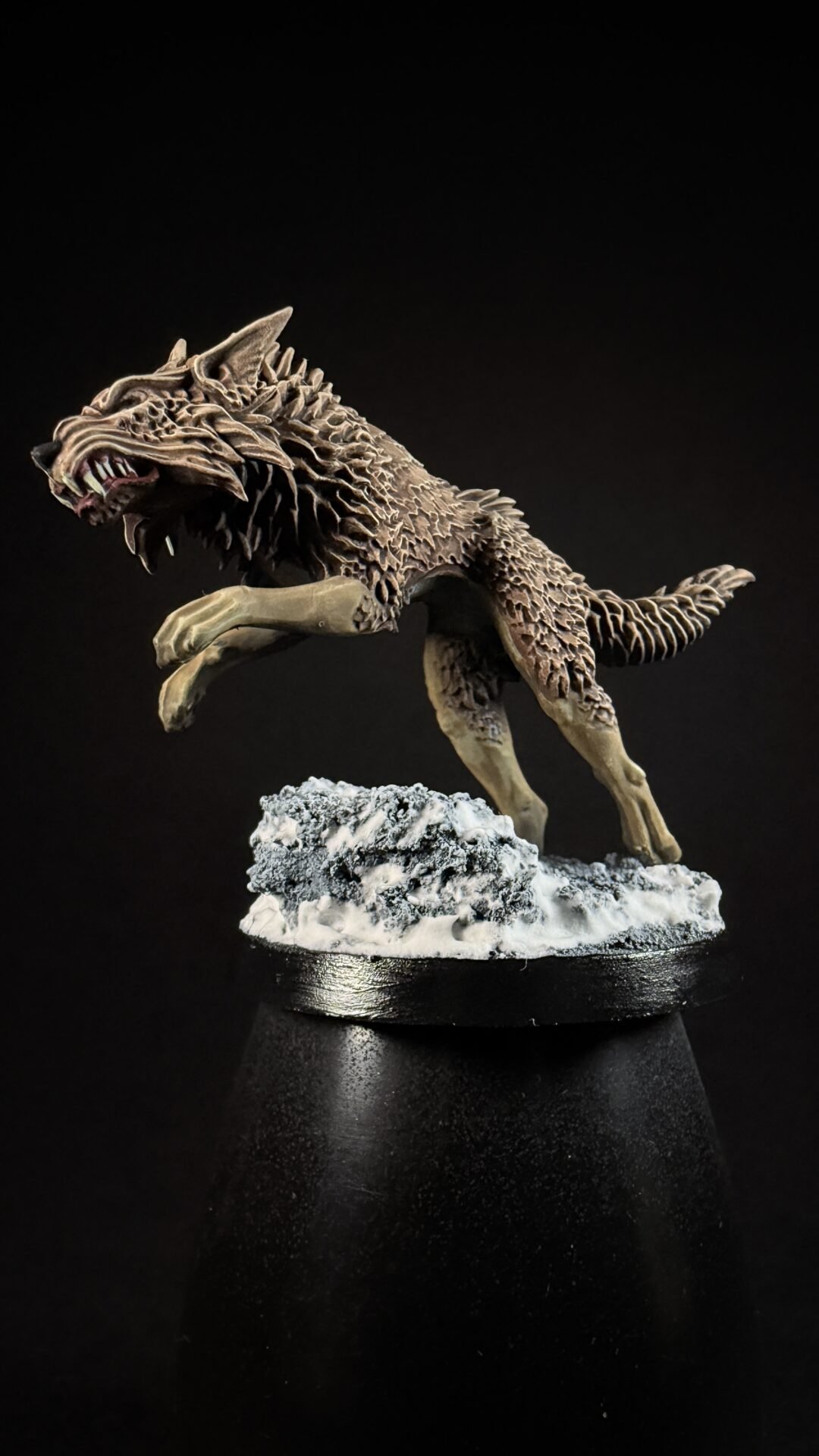 Fantasy wolf-like creature statue leaping on a snow-covered rocky base; detailed jagged fur and snarling jaws in a dark background.