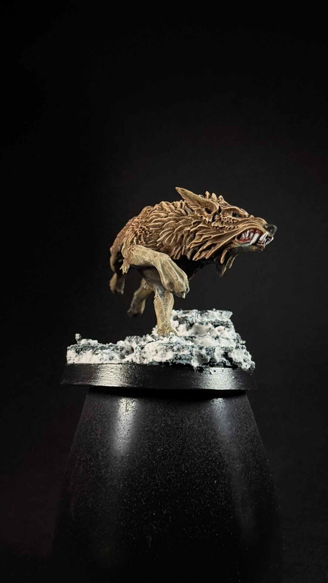 Brown, textured wolf-like miniature crouching on a snowy rocky base mounted on a display stand