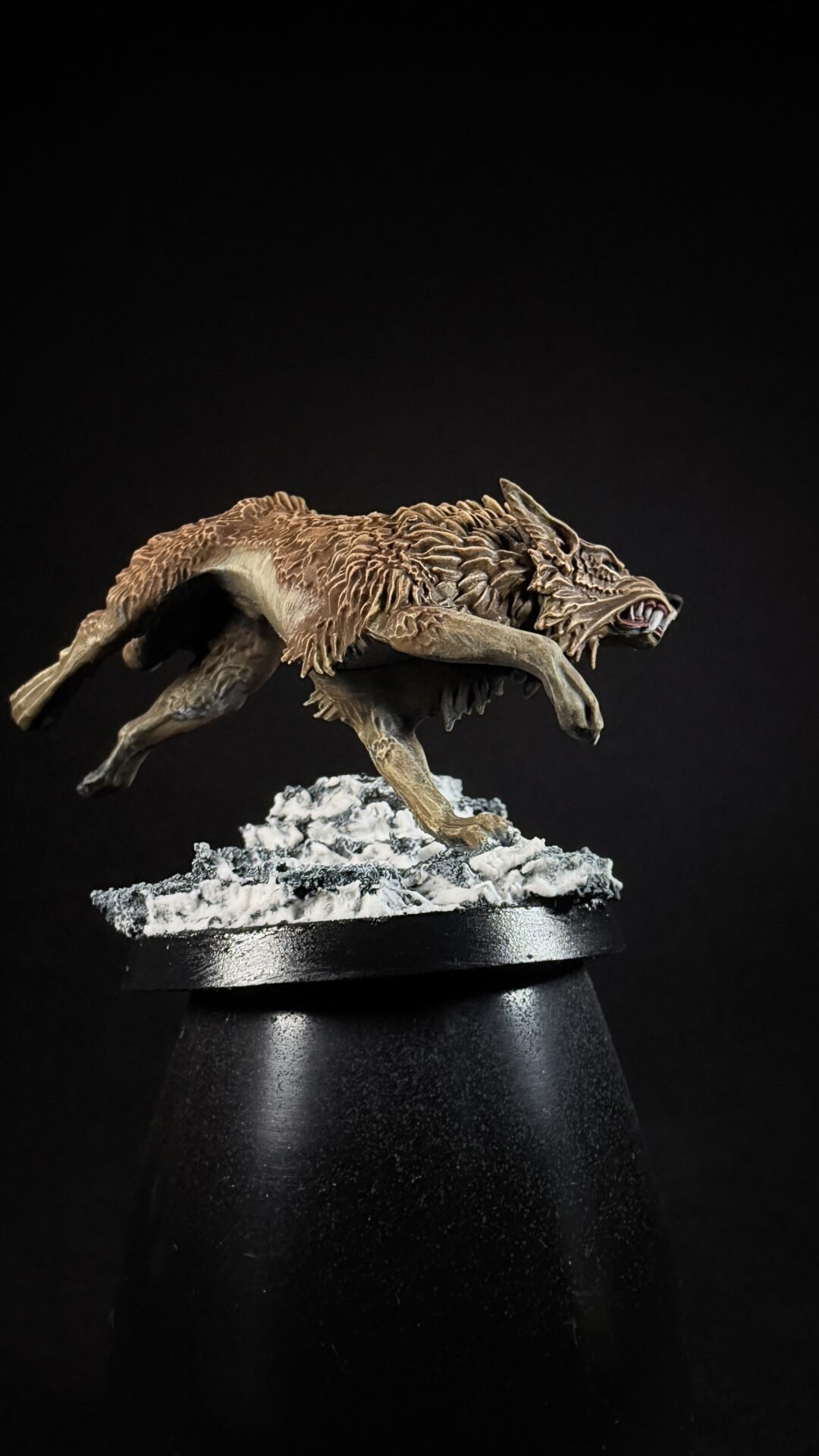 Bronze-toned sculpture of a snarling wolf in mid-leap, running on a snow-covered rocky base on a black pedestal