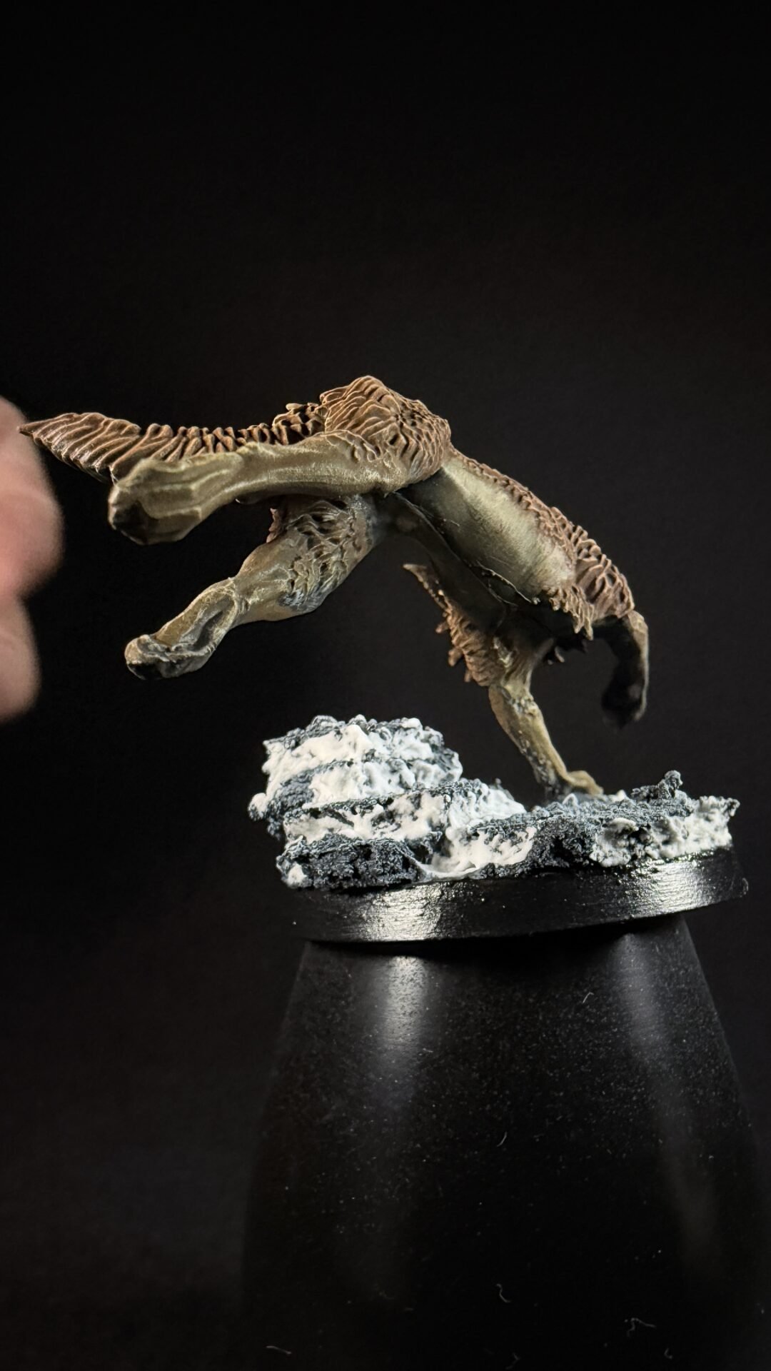 A dinosaur-like model perched on a rocky base, held by a hand against a black background.