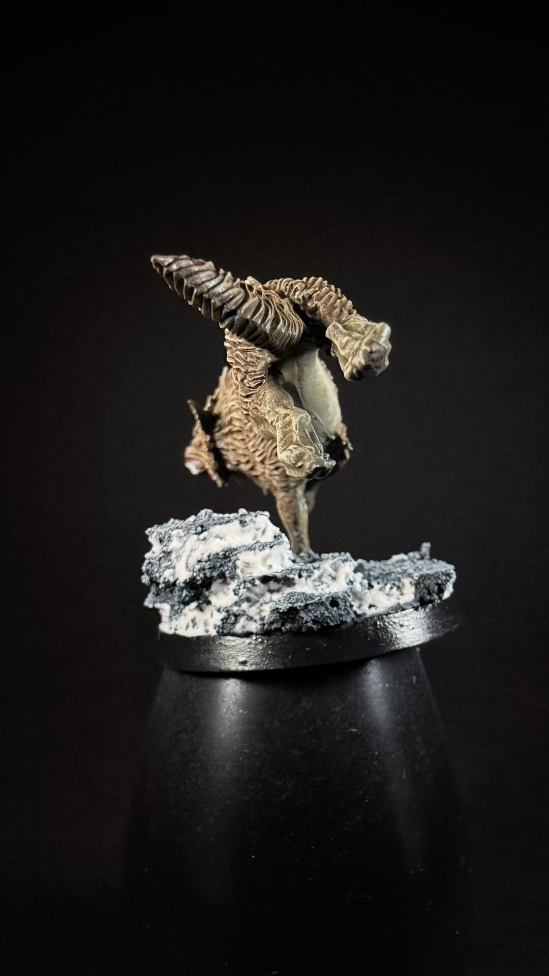 Detailed fantasy dragon miniature with large, curved wings perched on a rocky base against a black background.