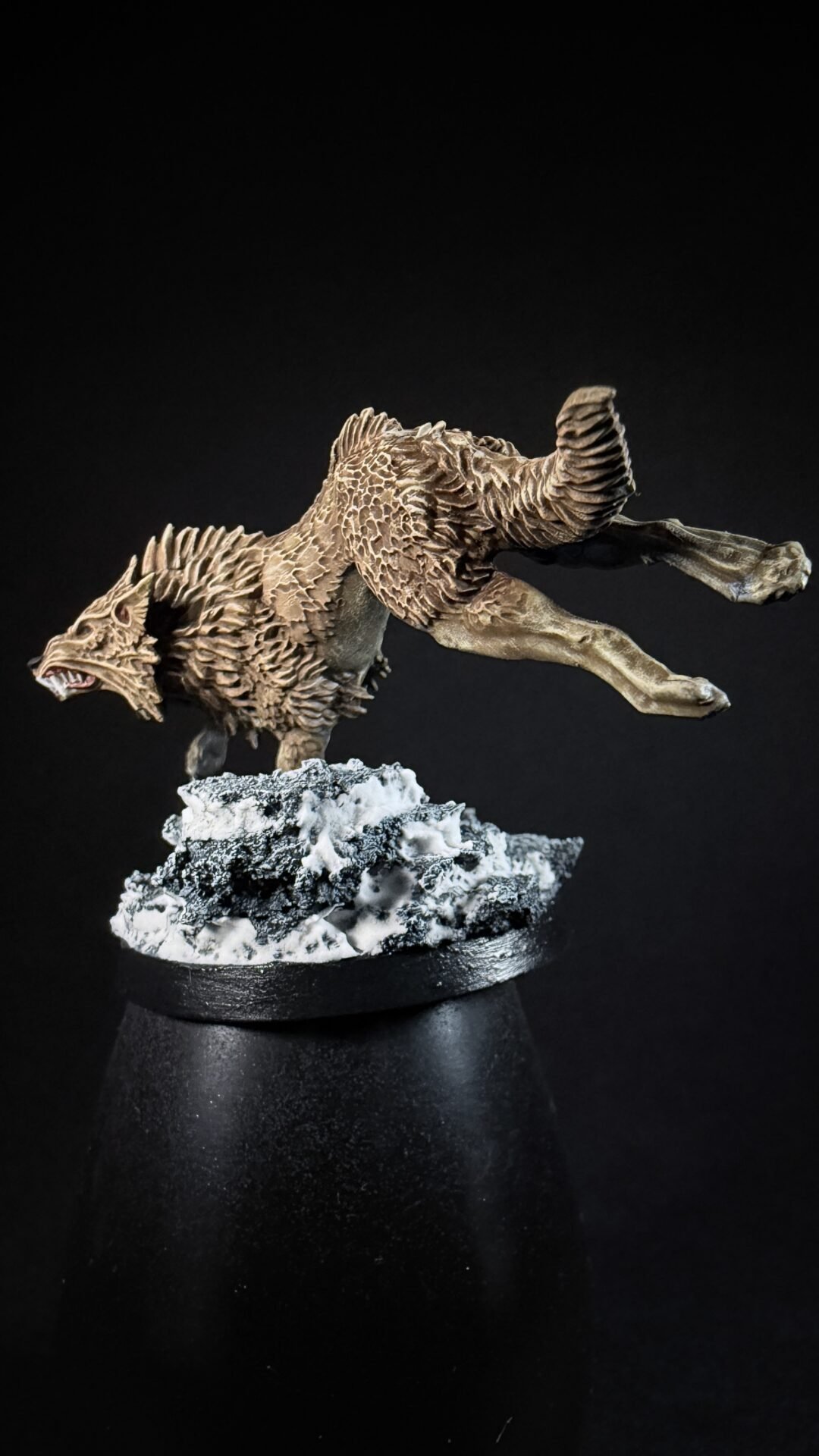 Werewolf miniature leaping forward with spiky fur, on a snow-dusted rocky base against a black background.