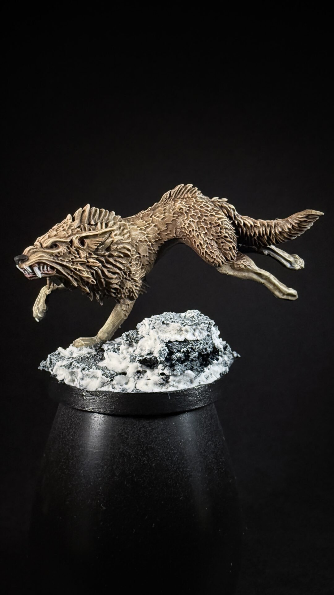 Textured wolf sculpture mid-leap, with rocky snow base on a black pedestal against a dark background