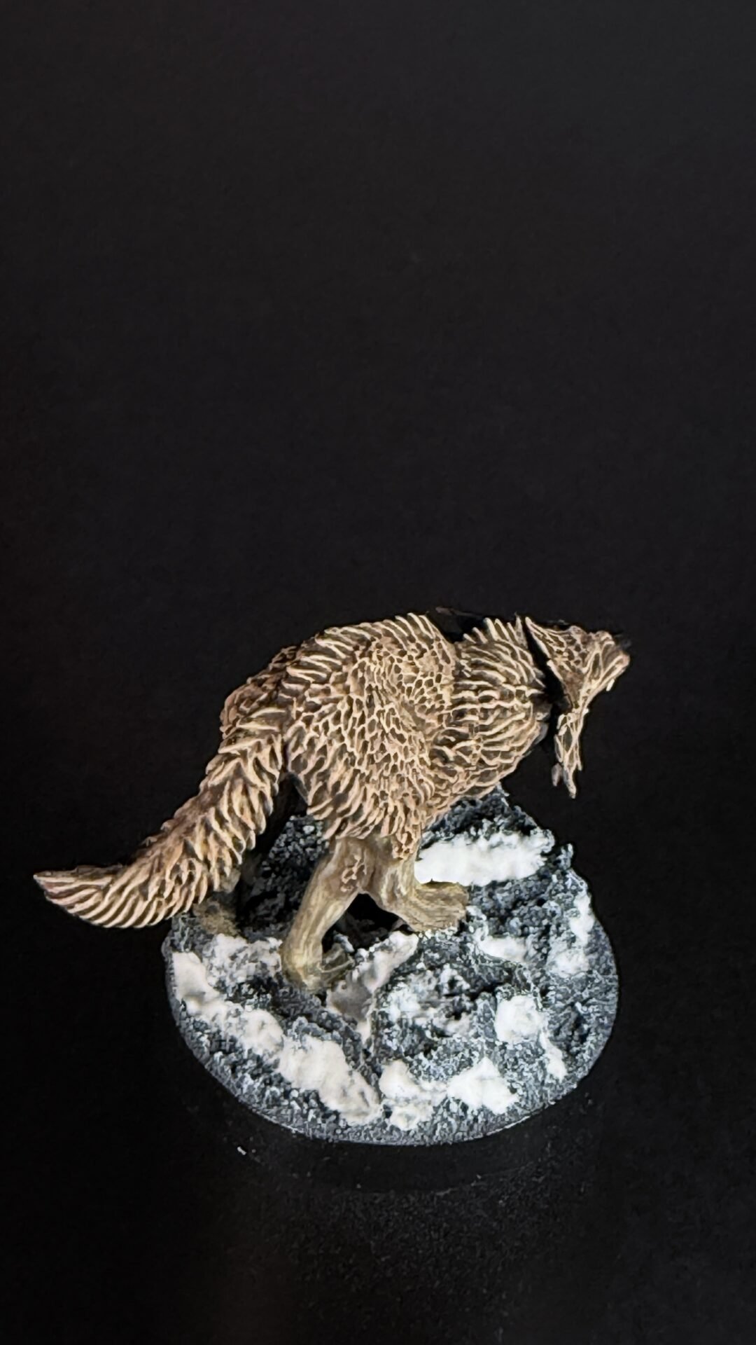 Sculpted wolf standing on a snowy rock with a dark background.