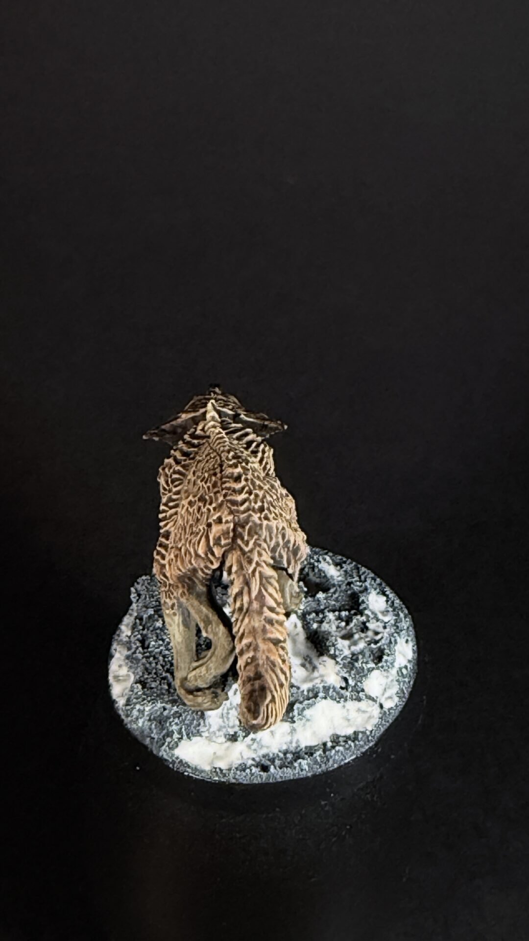 Brown, textured lizard sculpture perched on a rocky base against a dark background, with a snowy-looking rock surface.